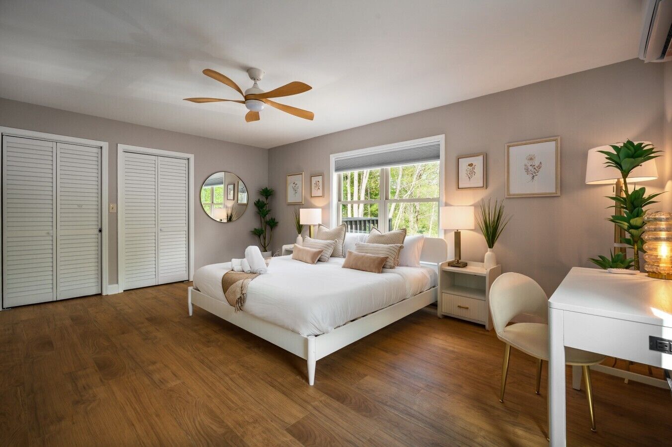 A bedroom with a bed, bedside tables, a desk, a chair, a ceiling fan, a window, and a mirror.