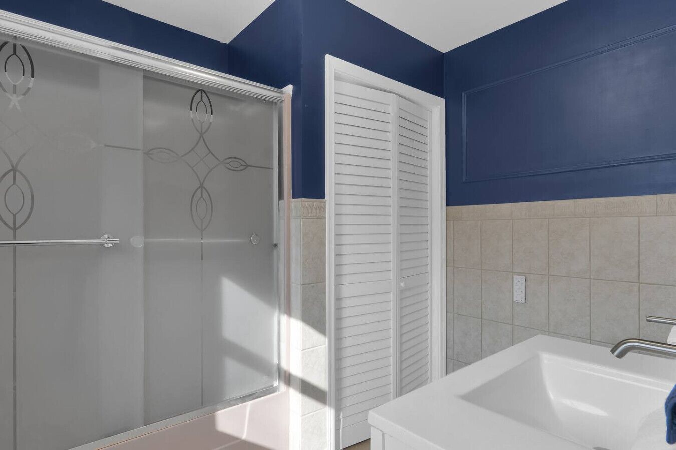 A bathroom with a shower, a sink, and a white door.