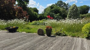Une terrasse en bois où une personne est allongée, entourée de verdure et de fleurs.