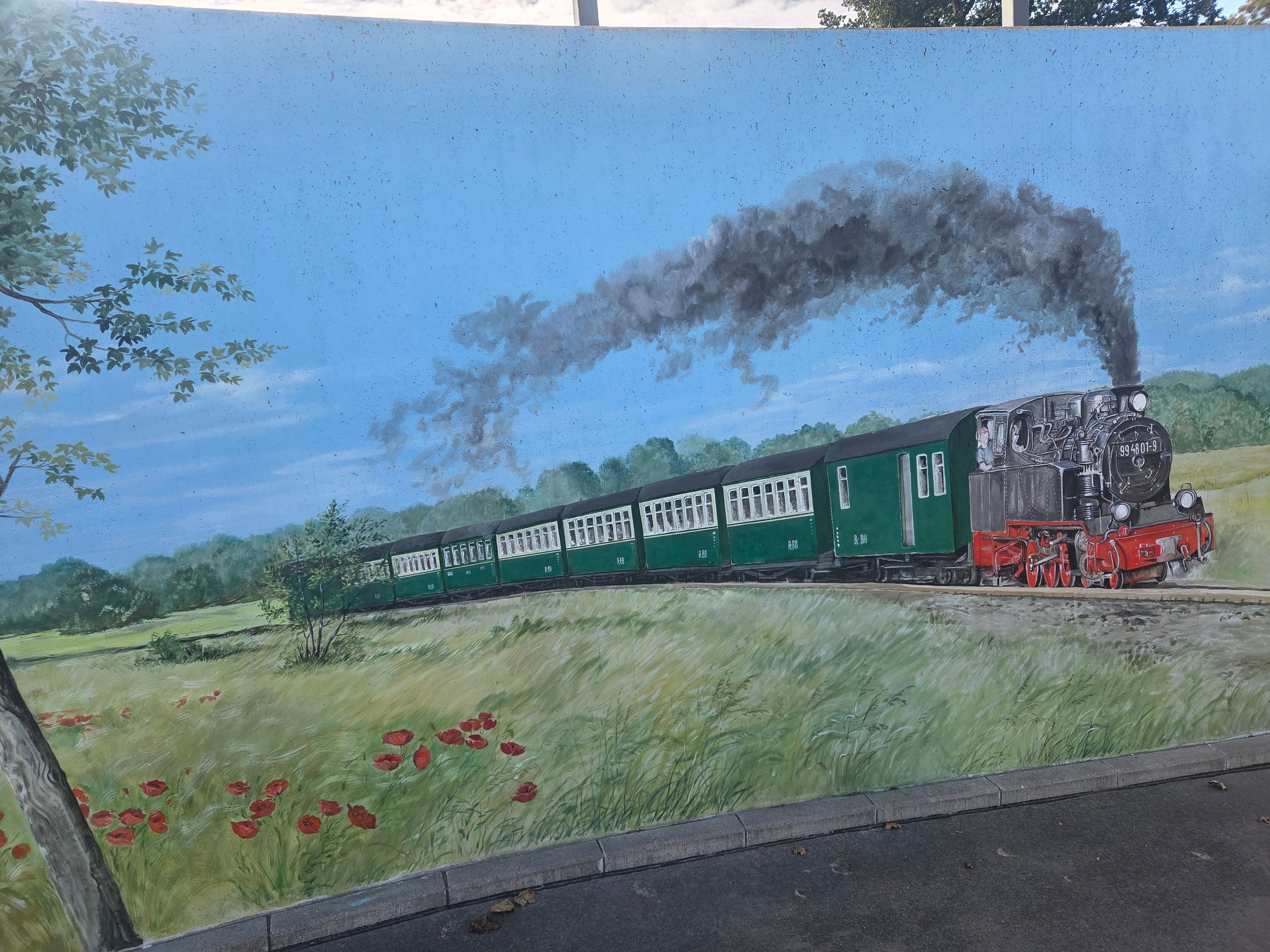 Un tren verde y negro con ventanales blancos y ruedas rojas, viajando sobre rieles.