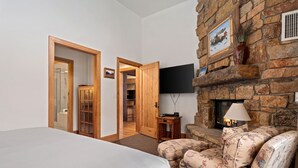 Un dormitorio con una cama, una puerta de madera, un televisor, una chimenea y un sillón estampado.