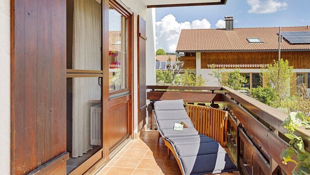 A balcony with a wooden floor, a sun lounger, and a view of a building with solar panels. - Apartment "Vogel" with Mountain View, Shared Garden, and Wi-Fi (Wertach)