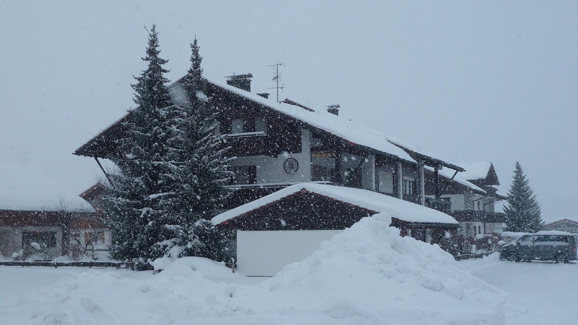 A multi-story building with a snow-covered roof and a large tree in front.