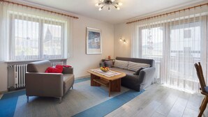 A living room with a sofa, a coffee table with fruit, a radiator, and sheer curtains. - Apartment "Vogel" with Mountain View, Shared Garden, and Wi-Fi (Wertach)