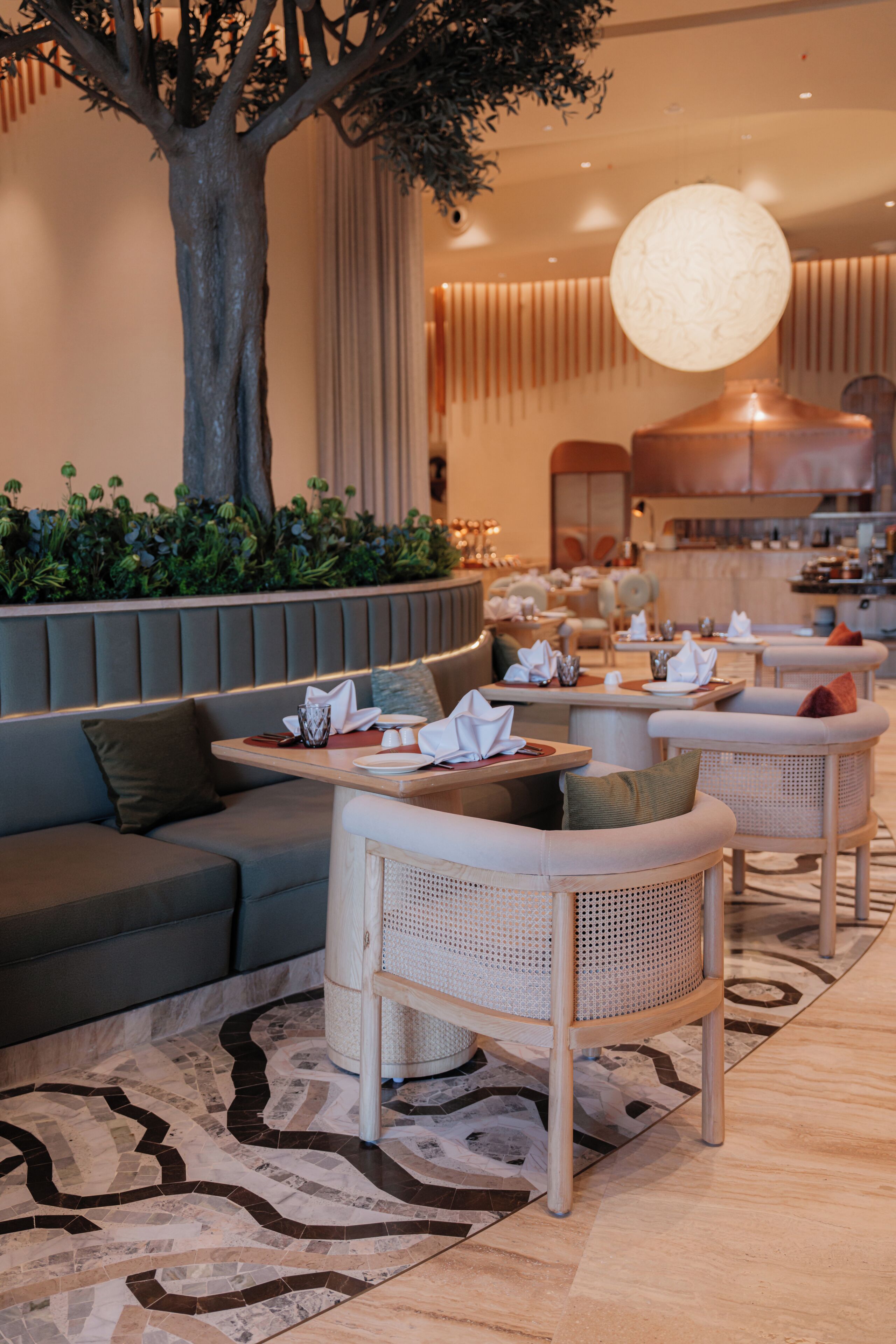 A modern lounge area with a large tree, cushioned seating, and a patterned floor.