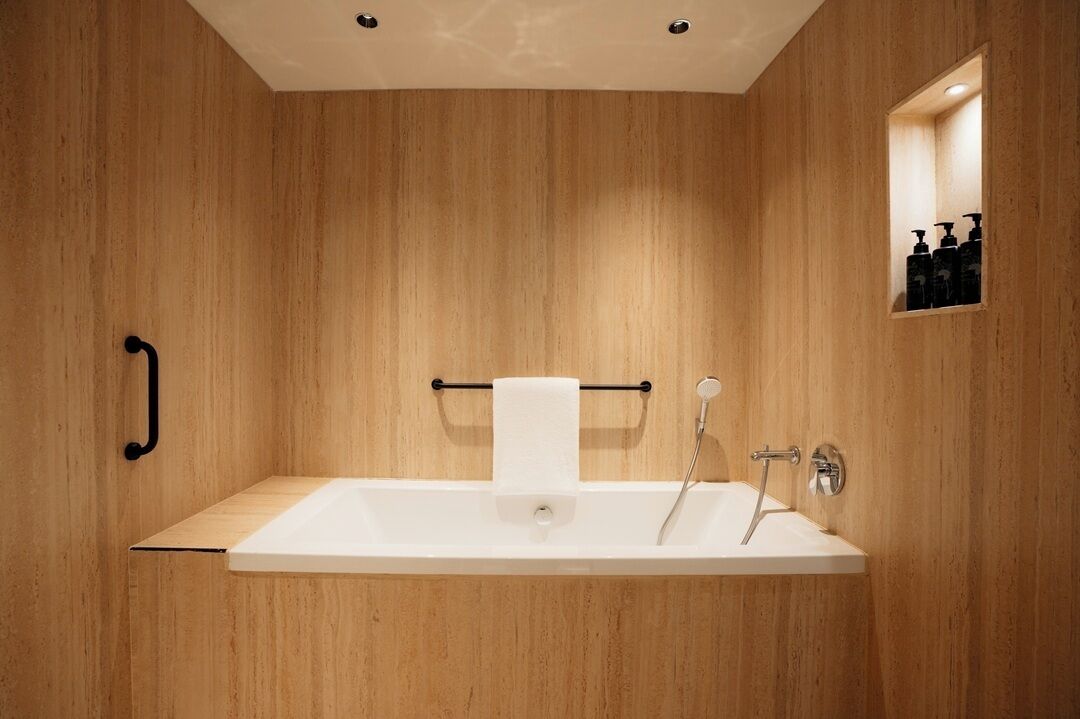 Une salle de bain moderne avec un mur en bois, une baignoire blanche, un porte-serviettes et un miroir agrémenté d’accessoires de toilette.