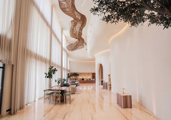 A spacious lobby with a long reception desk, seating area, and large windows allowing natural light.
