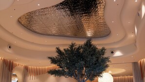 Eine geräumige Lobby mit einer zentralen Pflanze, Sitzbereichen und einem modernen Deckenstil.