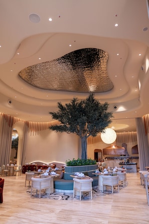 A spacious lobby with a central tree, seating areas, and a modern ceiling design.