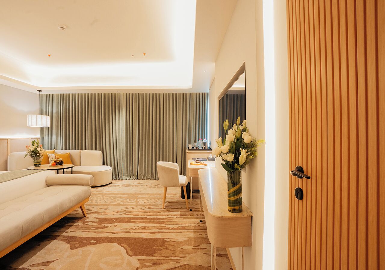 Una habitación de hotel moderna con sofá, sillón y una pequeña mesa con lámpara.