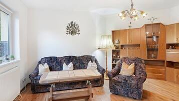 A living room with a sofa, armchair, wooden coffee table, and a chandelier.