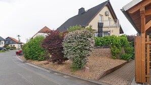 A residential street with houses, a driveway, and a garden with various shrubs. - Holiday Home 'Ferienwohnung Sehr Ruhig' with Private Garden and Wi-Fi (Pößneck)