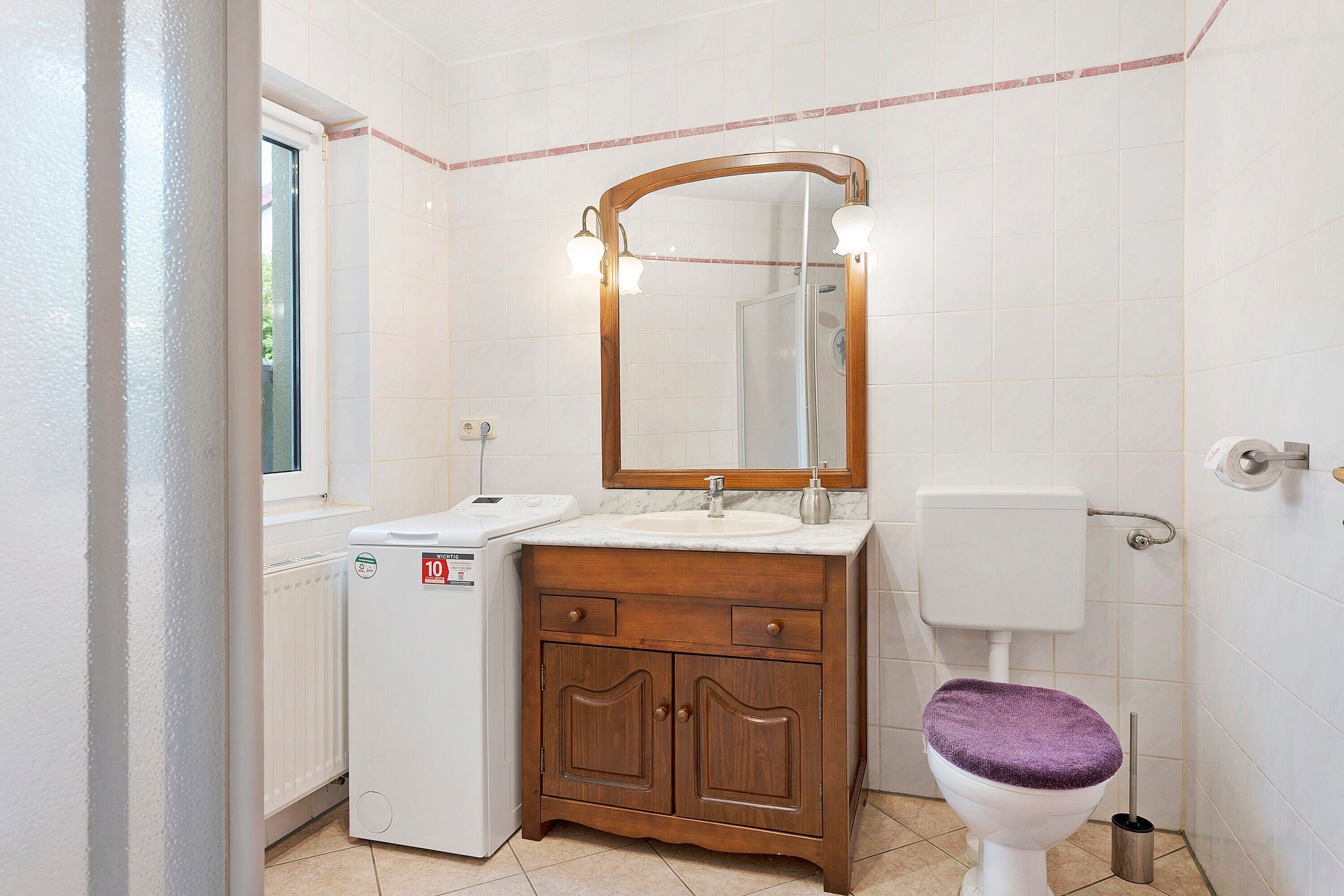 Un baño con inodoro blanco, tocador de madera con espejo y una lavadora pequeña.