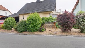 A residential house with a dark roof, a beige facade, and a front yard with various shrubs and a small tree. - Holiday Home 'Ferienwohnung Sehr Ruhig' with Private Garden and Wi-Fi (Pößneck)