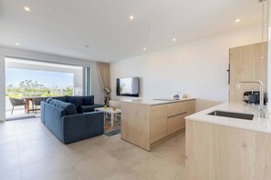 Eine moderne Küche mit integrierter Kochinsel, einem Essbereich mit Sofa und Tisch und einem großen Fenster mit Blick.