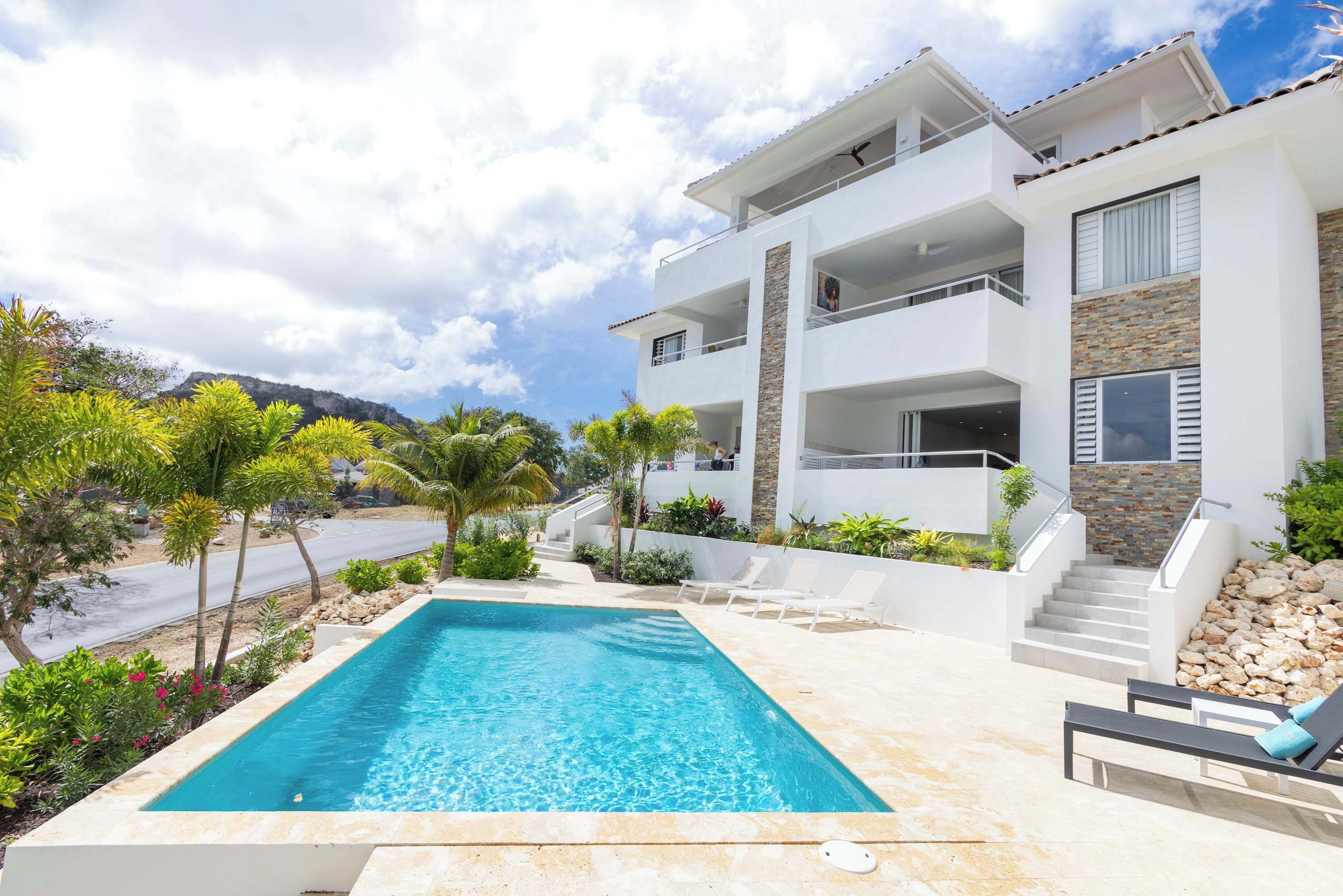 A modern two-story house with a swimming pool, outdoor seating, and a staircase leading to the upper floor.