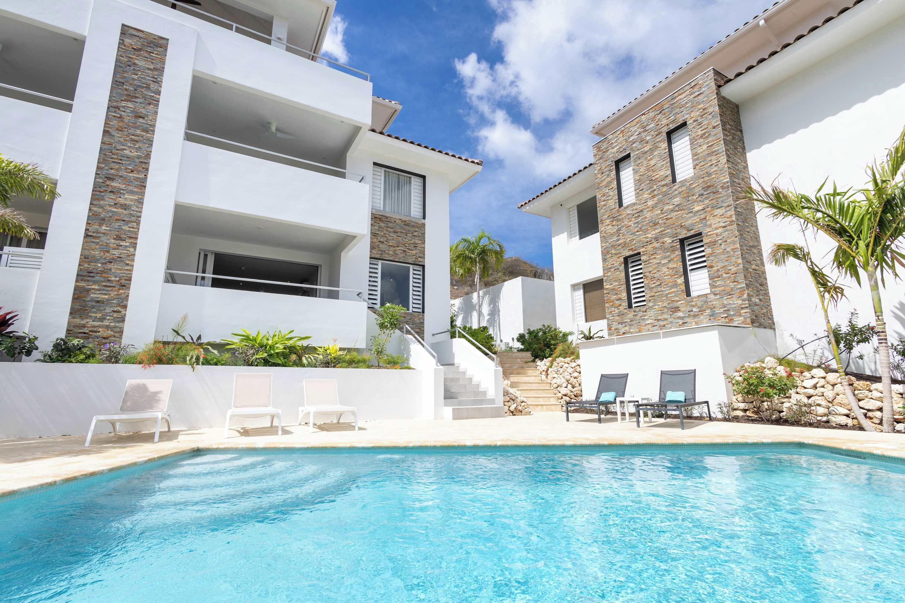 Un hôtel moderne doté d’une piscine, de balcons blancs et d’éléments décoratifs en pierre.