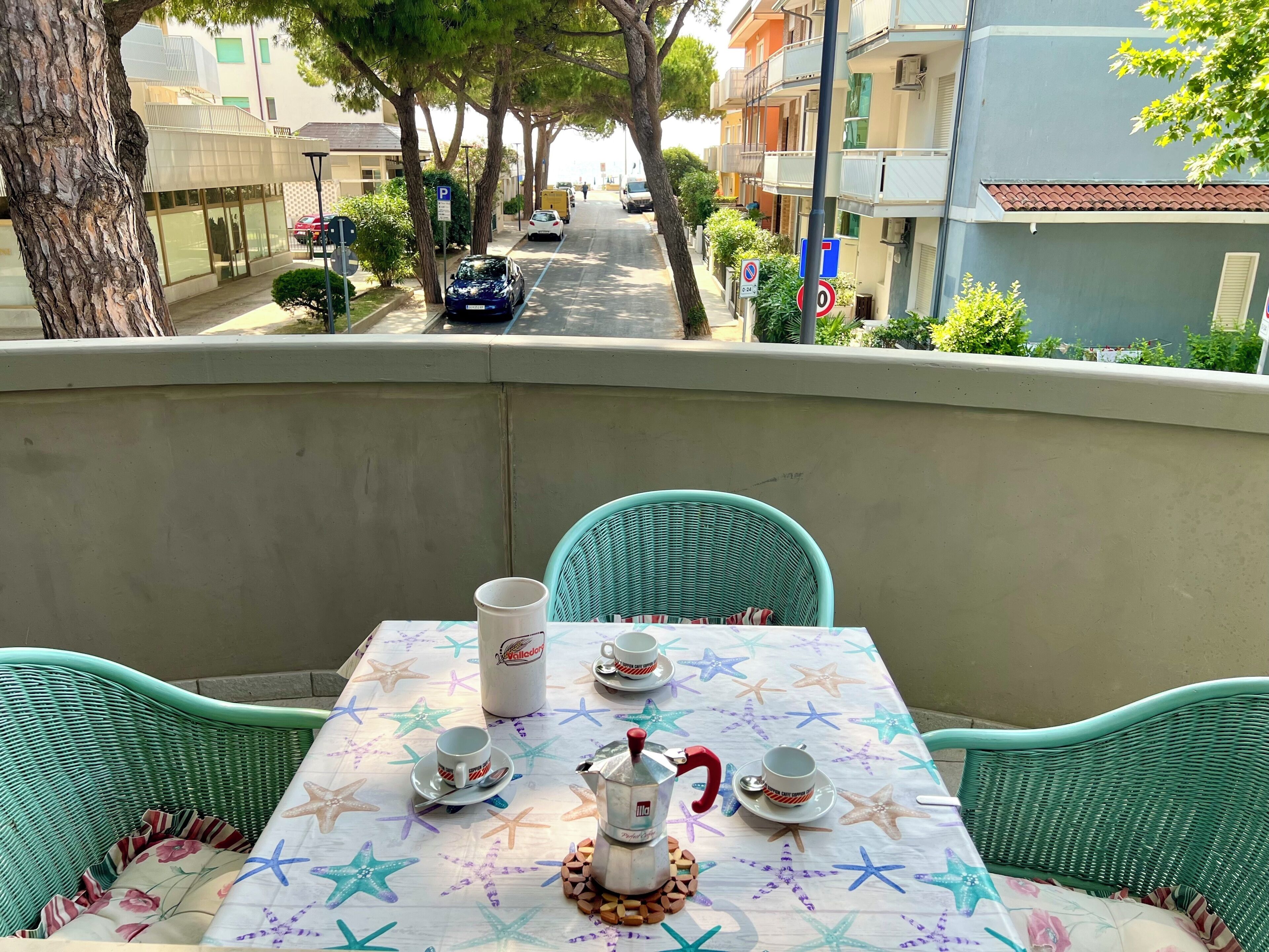 A balcony with a table set for two, featuring a star-patterned tablecloth, a coffee pot, and two cups.
