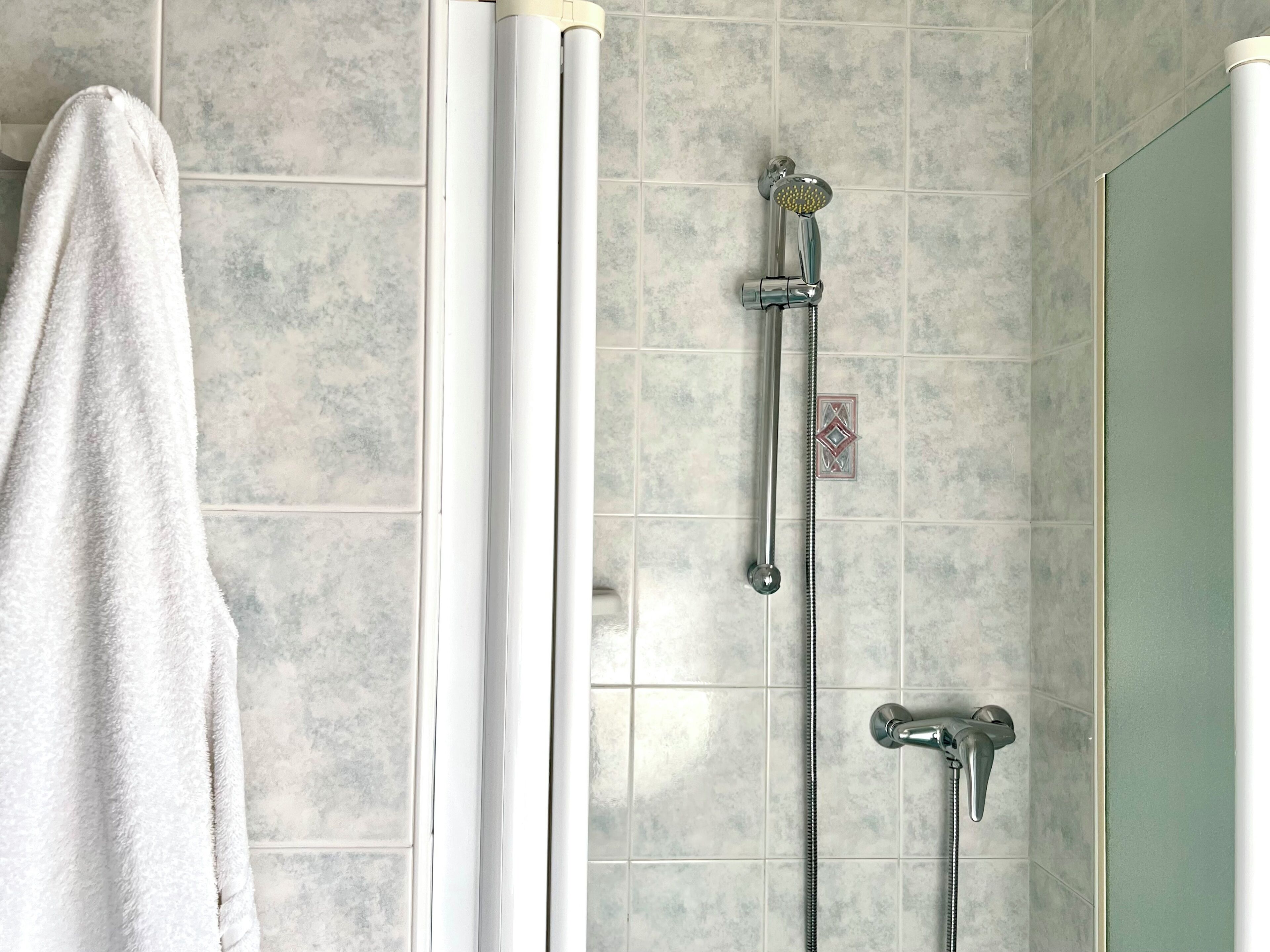 Ein Badezimmer mit Dusche, Handtuch und Fliesenwand.