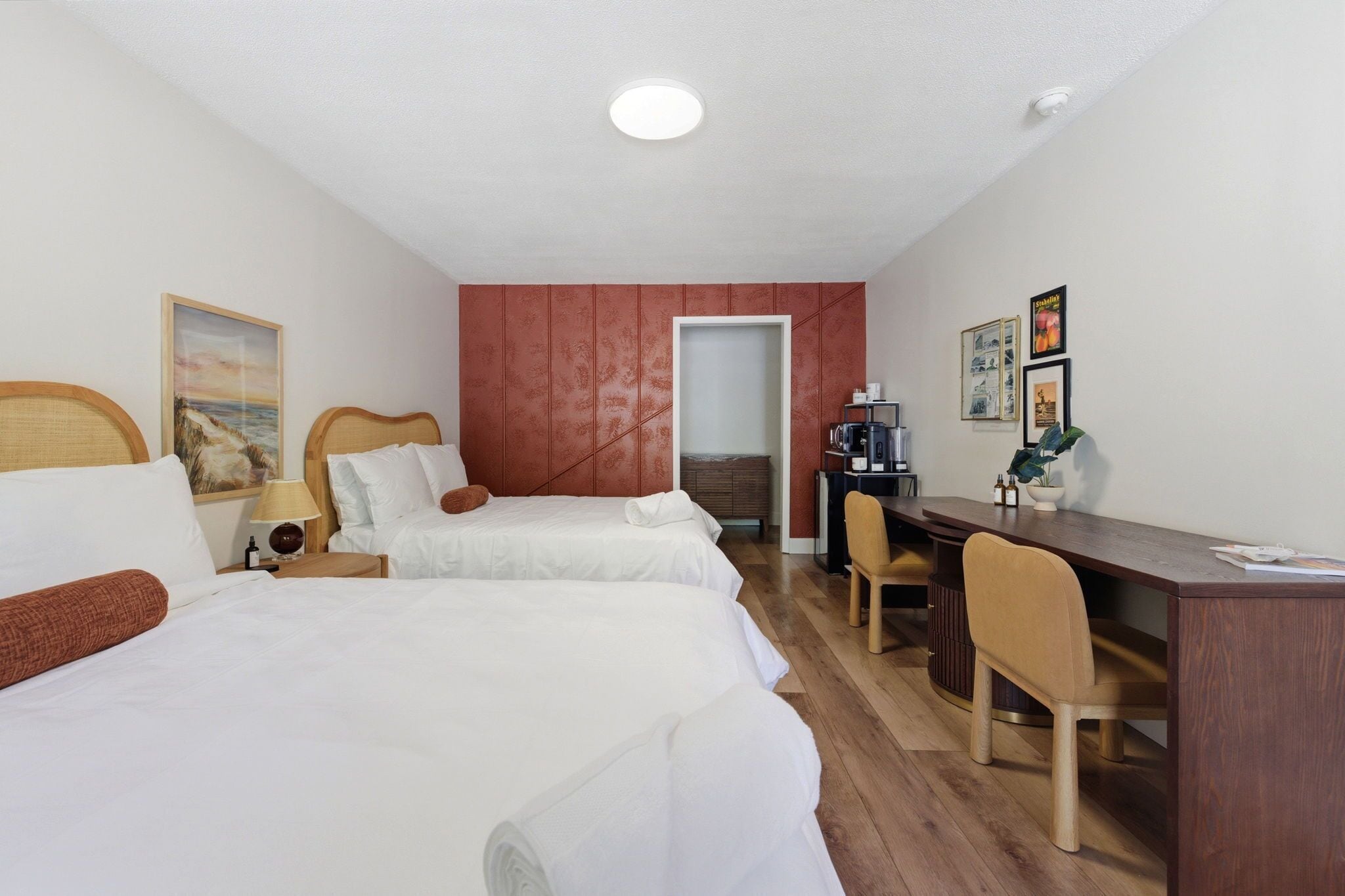 A hotel room with two beds, a desk, a chair, a coffee machine, and a door leading to a balcony.