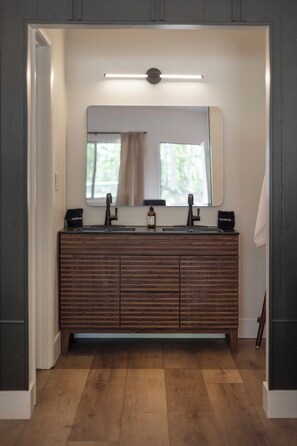 Un baño con tocador de madera, un espejo grande y una lámpara sobre el espejo.