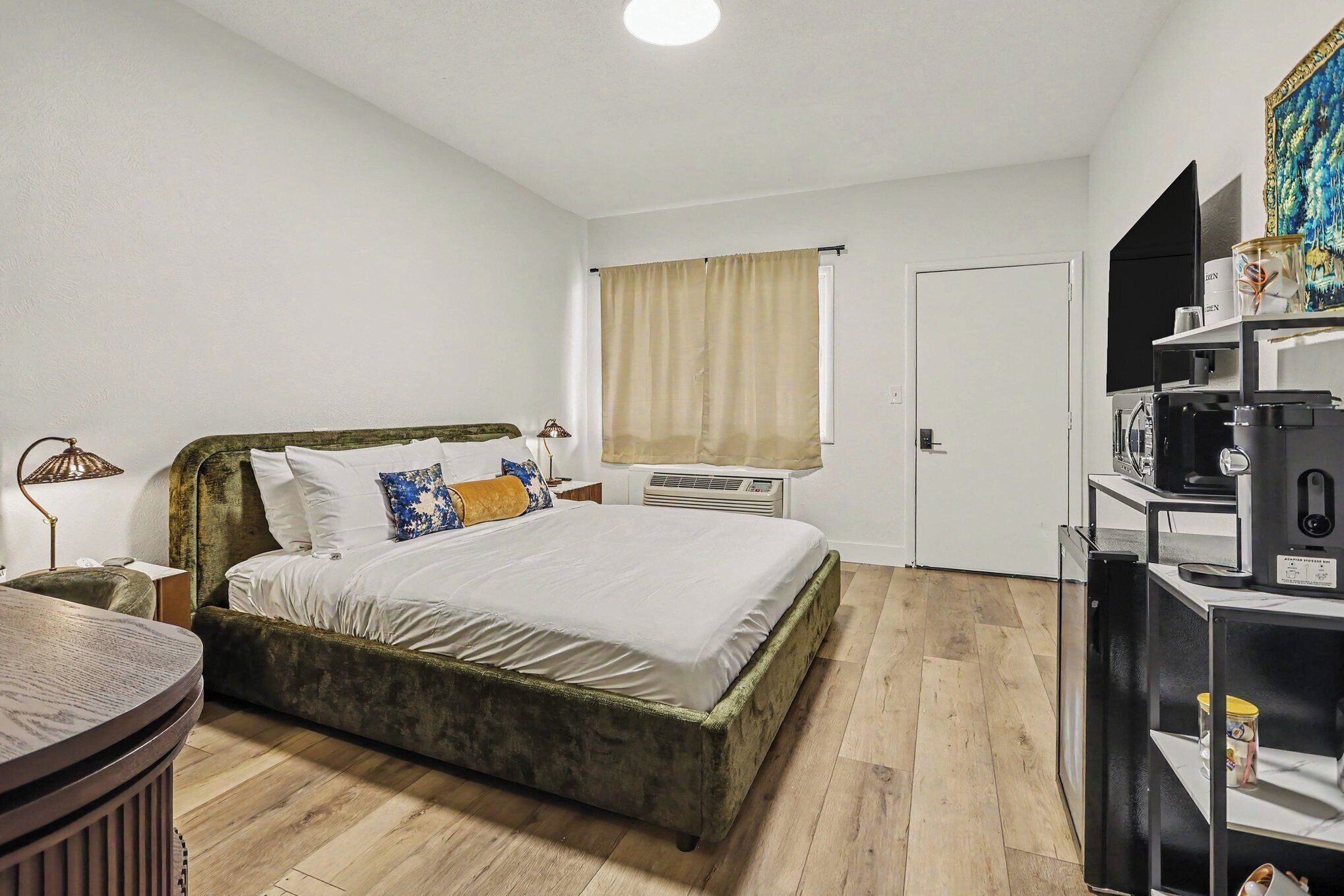 Een slaapkamer met een bed, nachtkastje, lamp, airconditioning en een televisie op een standaard.