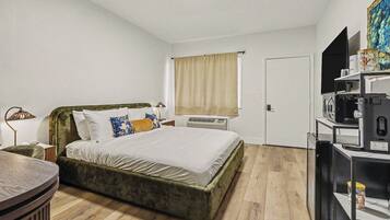 Een slaapkamer met een bed, nachtkastje, lamp, airconditioning en een televisie op een standaard.