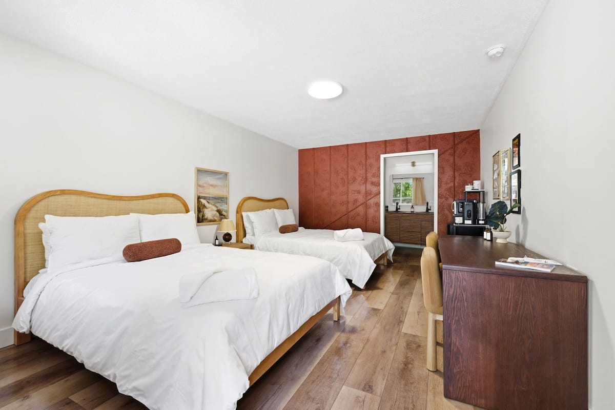 Una habitación de hotel con dos camas, un escritorio y una puerta que da a un baño.