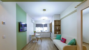 A compact living space with a kitchenette, a dining area, and a sofa with cushions. - Cozy & Modern Apartment Near Arena Mall, Free Parking, Wi-Fi ,Ac. (Bacau)
