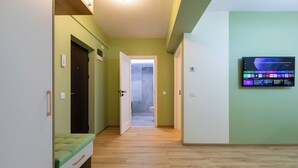 A hallway with a bed, a TV mounted on the wall, and a door leading to a bathroom. - Cozy & Modern Apartment Near Arena Mall, Free Parking, Wi-Fi ,Ac. (Bacau)
