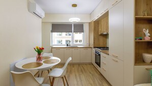 A modern kitchen with a dining area, a window with blinds, a built-in stove, and a small shelf with decorative items. - Cozy & Modern Apartment Near Arena Mall, Free Parking, Wi-Fi ,Ac. (Bacau)