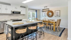 A modern kitchen with white cabinets, a central island with stools, a dining area with wooden furniture, and a large decorative mirror on the wall. - Lakefront Retreat w/ Boat Dock, Hot Tub & Large Game Room!  Sleeps 10 (Denver)