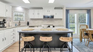A modern kitchen with white cabinets, a central island with stools, a microwave, and a large window with blinds. - Lakefront Retreat w/ Boat Dock, Hot Tub & Large Game Room!  Sleeps 10 (Denver)