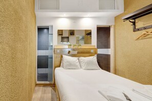 Een slaapkamer met een bed, een houten hoofdbord, een spiegel, een klein plankje met boeken en een handdoek op het bed.
