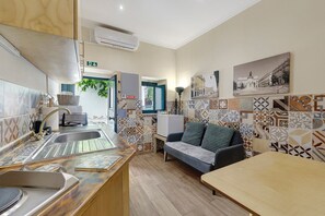 Una cocina con lavabo, refrigerador y comedor con mesa y sofá.