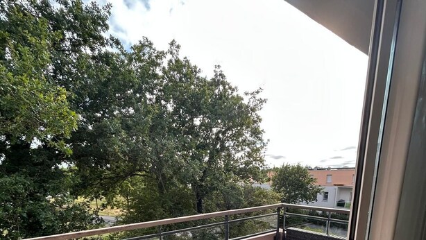 Uma varanda com grama sintética, móveis de vime e guarda-corpo de vidro.