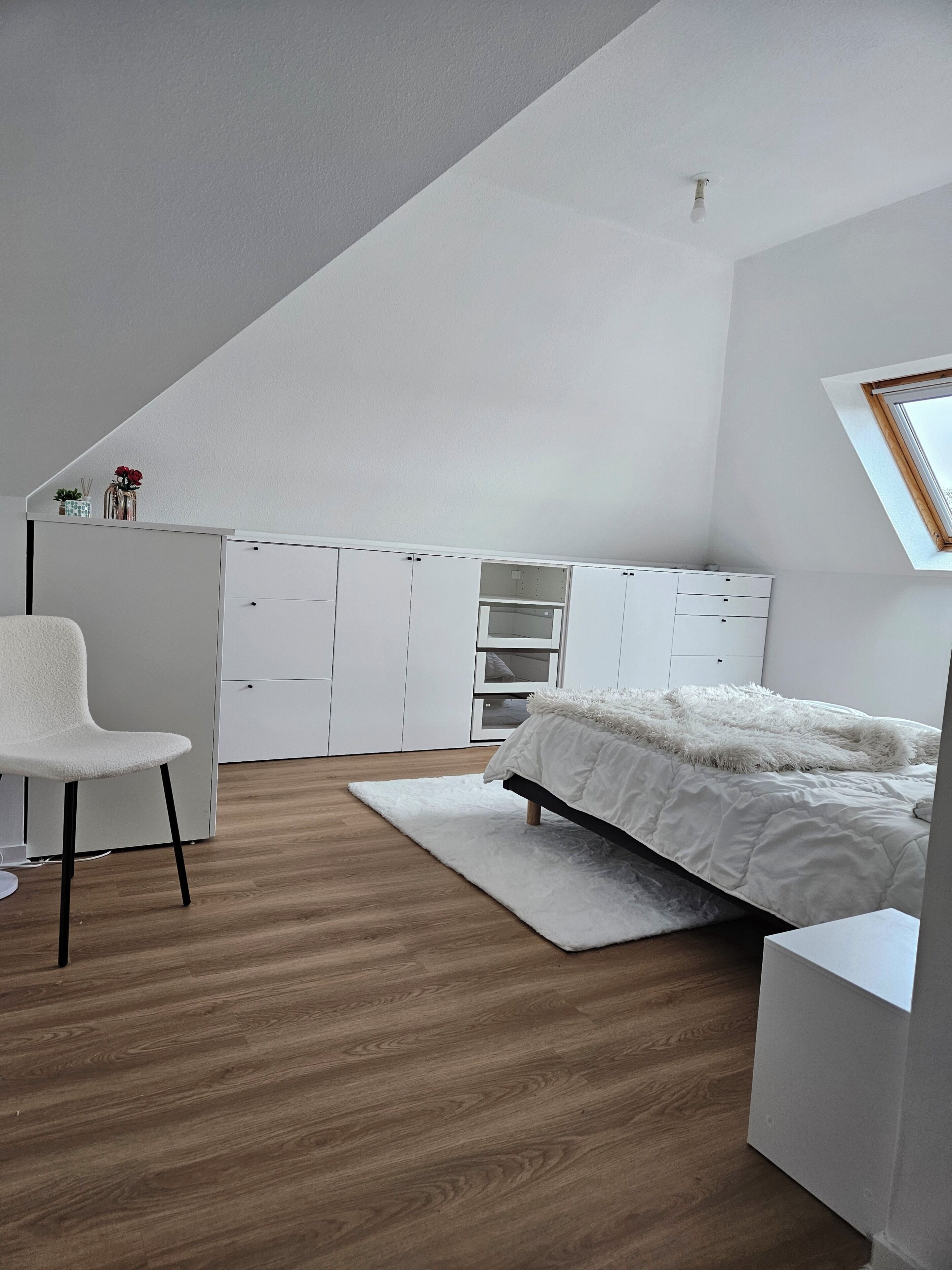 Een slaapkamer met een schuine kap, een bed, een bureau en een stoel.