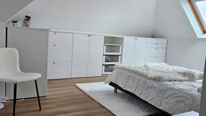 Quarto com teto inclinado, cama, escrivaninha e cadeira.