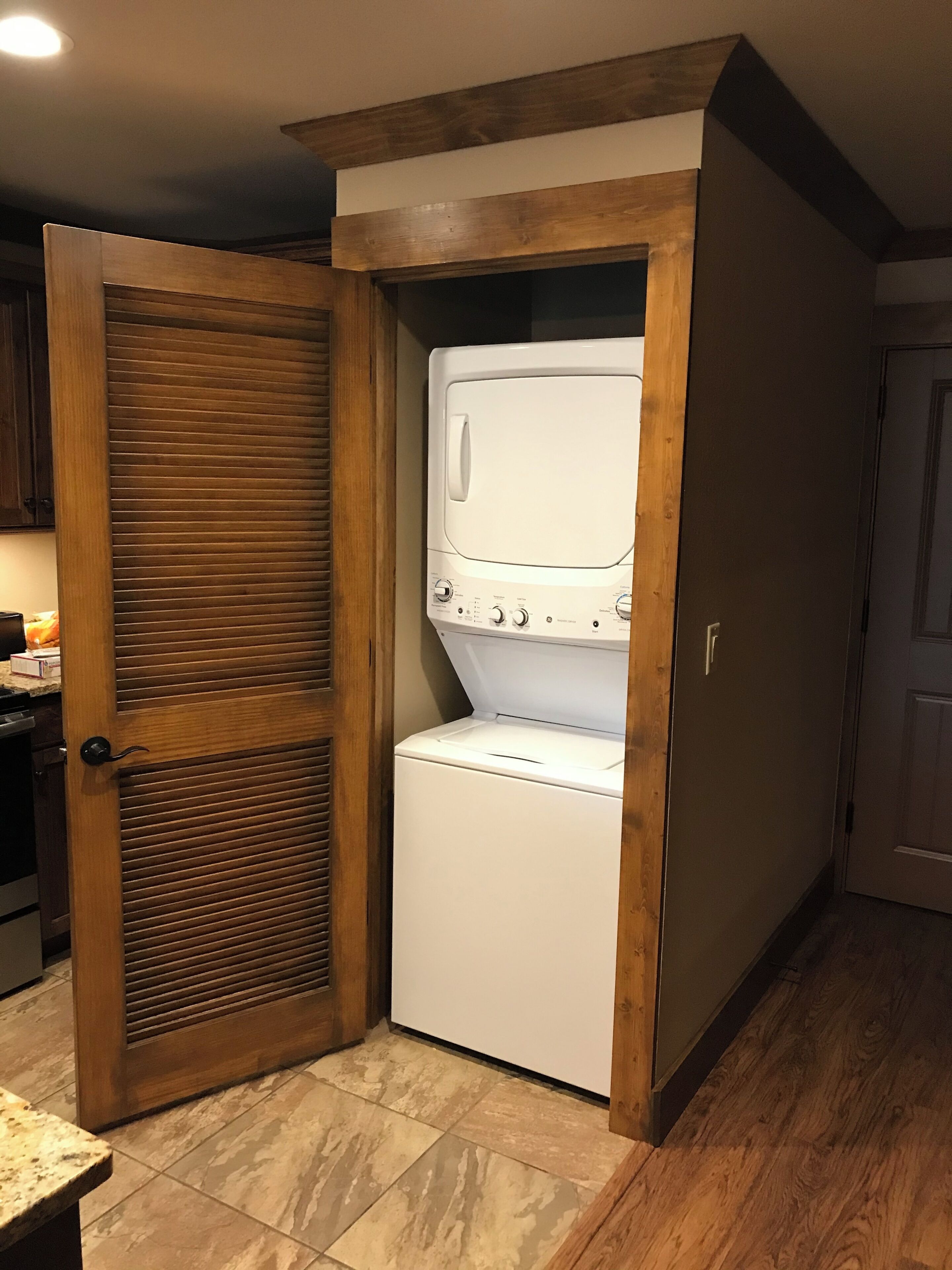 A compact laundry room with a built-in washer and dryer, wooden cabinetry, and a tiled floor.