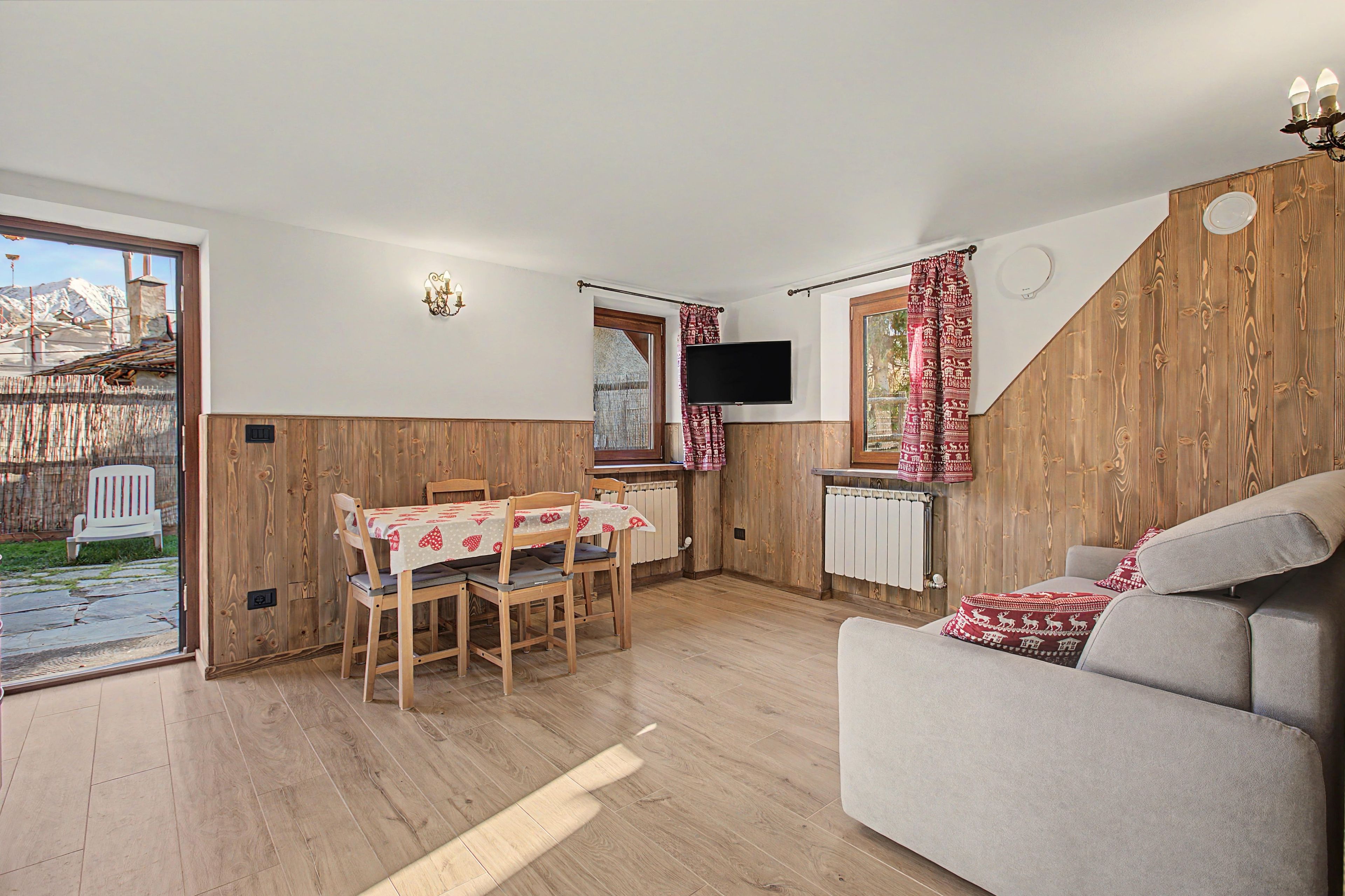 Una sala de estar acogedora con un sofá, una mesa de comedor con sillas, un televisor y vistas al exterior.