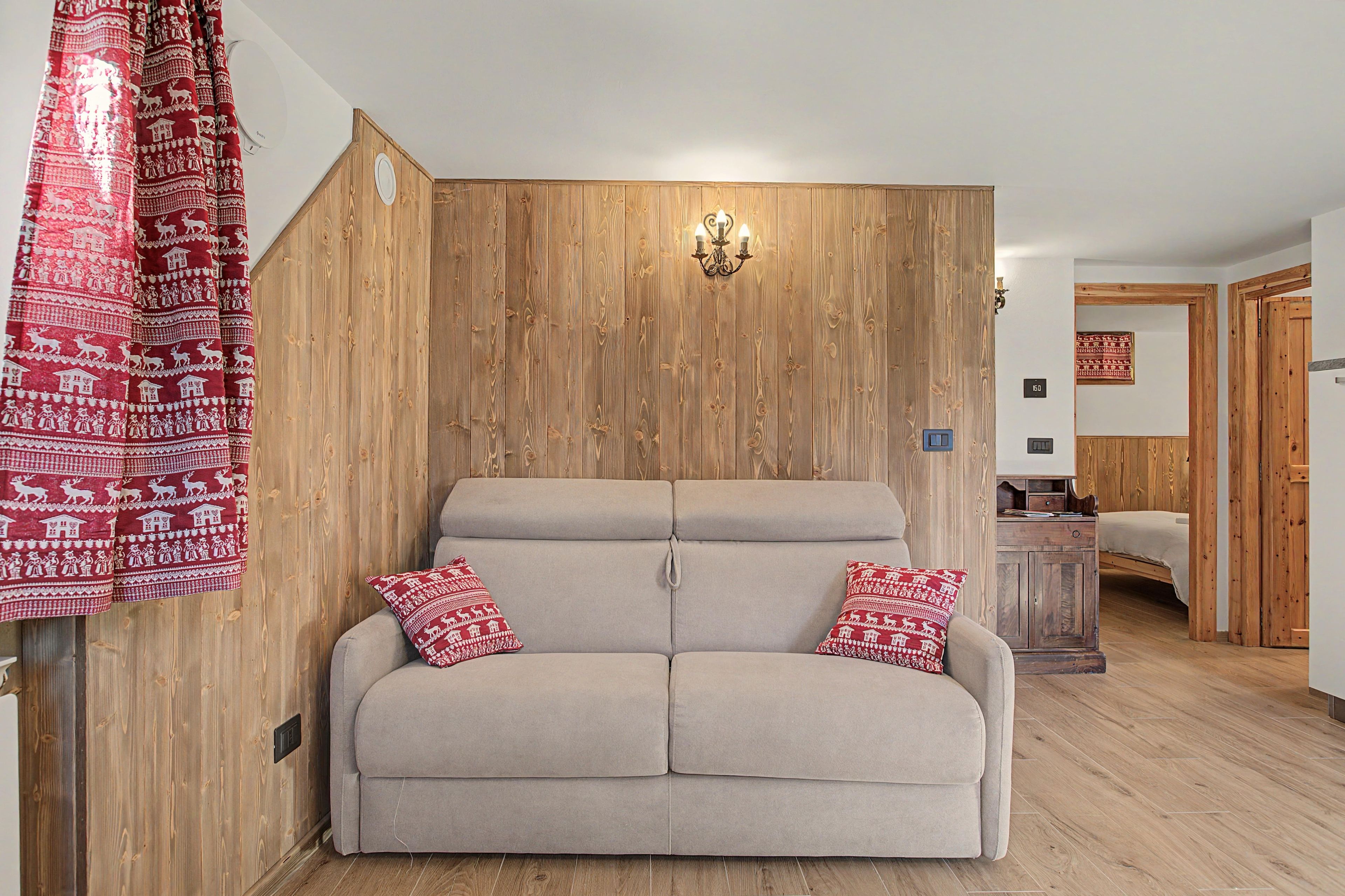 Un sofá de tonos neutros con dos almohadones decorativos frente a una pared de madera con una lámpara empotrada.