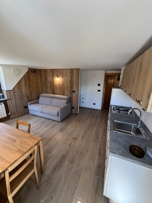A compact kitchen with a built-in stove, a sink, and a wooden dining table. - Apartment 'L’angolo del paradiso Gimillan' with Mountain View and Private Garden (Gimillan)