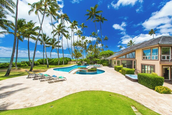 A pool with lounge chairs, palm trees, and a house with large windows.