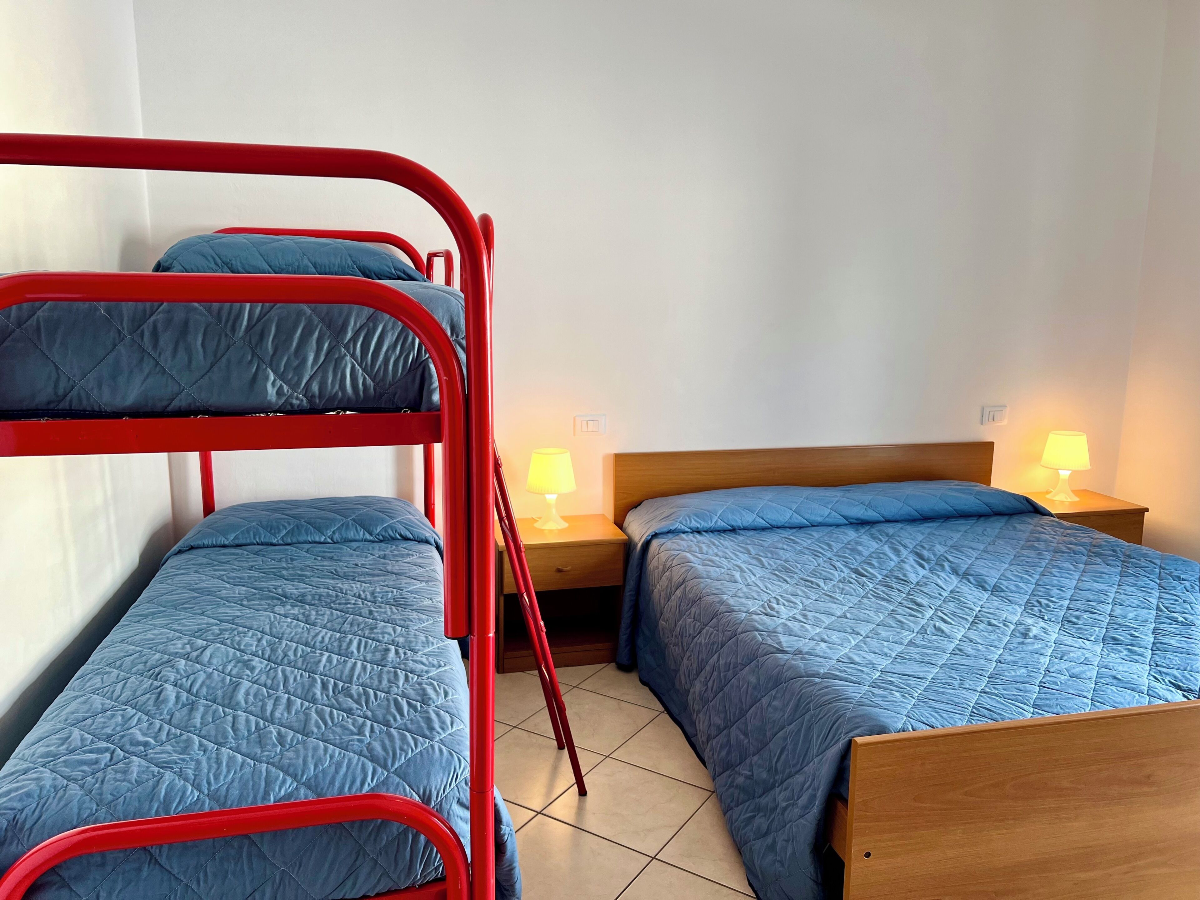 Una habitación con literas, una cama de madera y dos lámparas de noche.