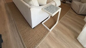 Ein Wohnzimmer mit einer Couch, einem Fernseher und einem Gemälde, das eine Strandansicht zeigt.