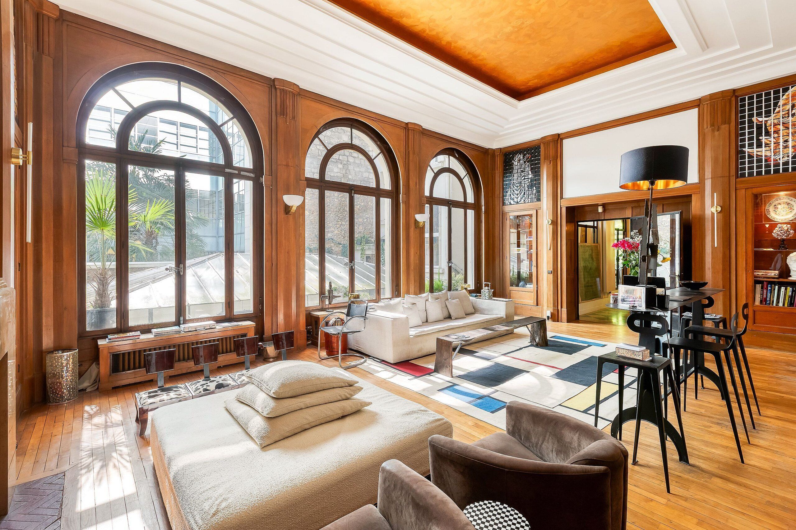 A spacious living room with large arched windows, a sofa, a coffee table, and a dining area with chairs and a lamp.