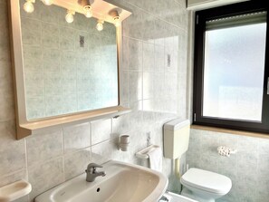 A bathroom with a sink, mirror, toilet, and window. - Familiar Apartment Close to the Beach (Lignano Sabbiadoro)