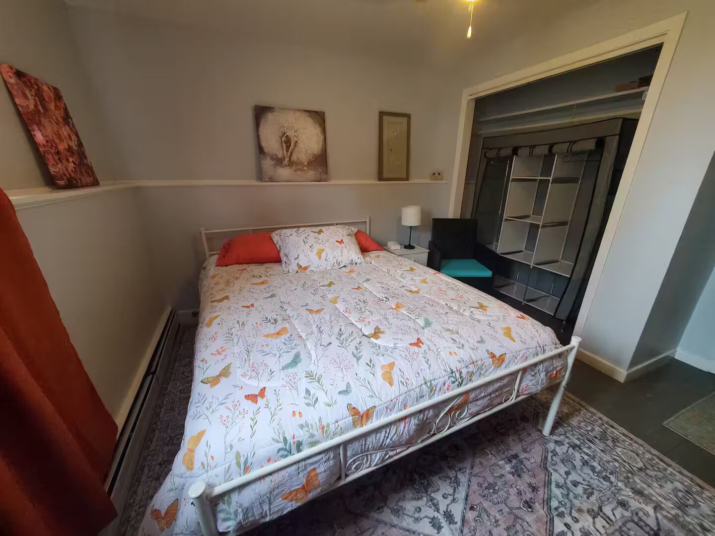 Een slaapkamer met een bed, een nachtkastje, een stoel, een deur en een muur met een schilderij.