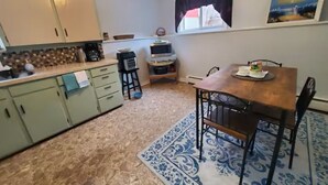 Una cocina con gabinetes verdes, una mesa de comedor con sillas, un tapete azul estampado y un cuadro en la pared.