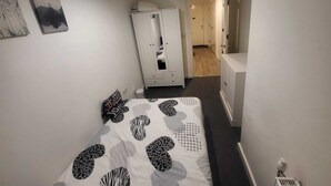 Et aflangt værelse med en seng, et skab og en dør til et andet værelse.